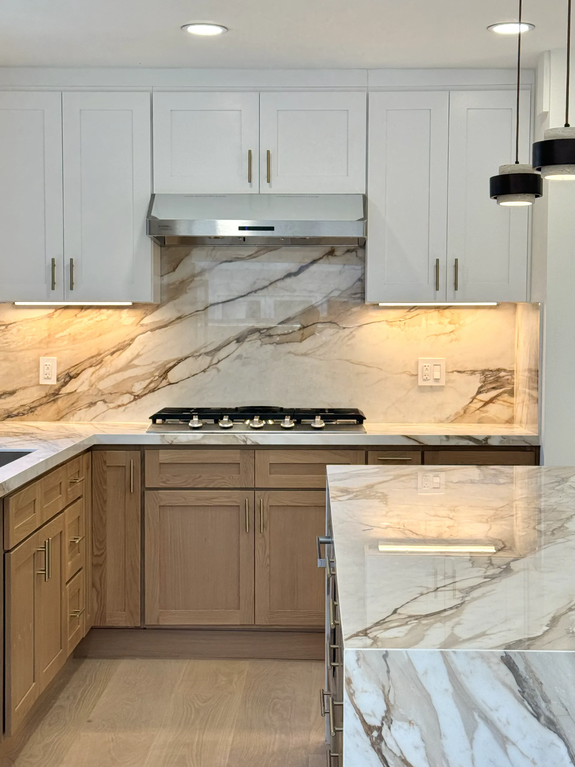 Two-tone kitchen with white upper cabinets, wood lower cabinets, and full-height stone surfaces