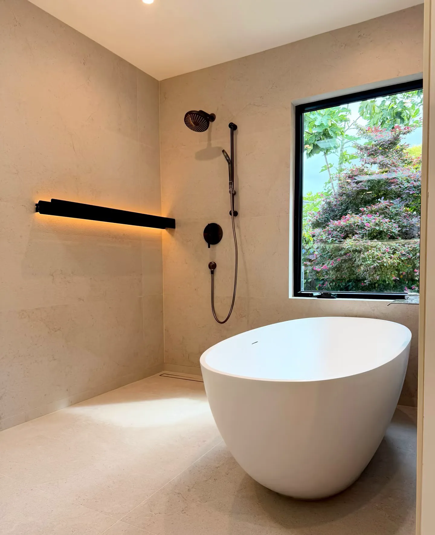 Freestanding bathtub beside a wall-mounted shower and a large garden window