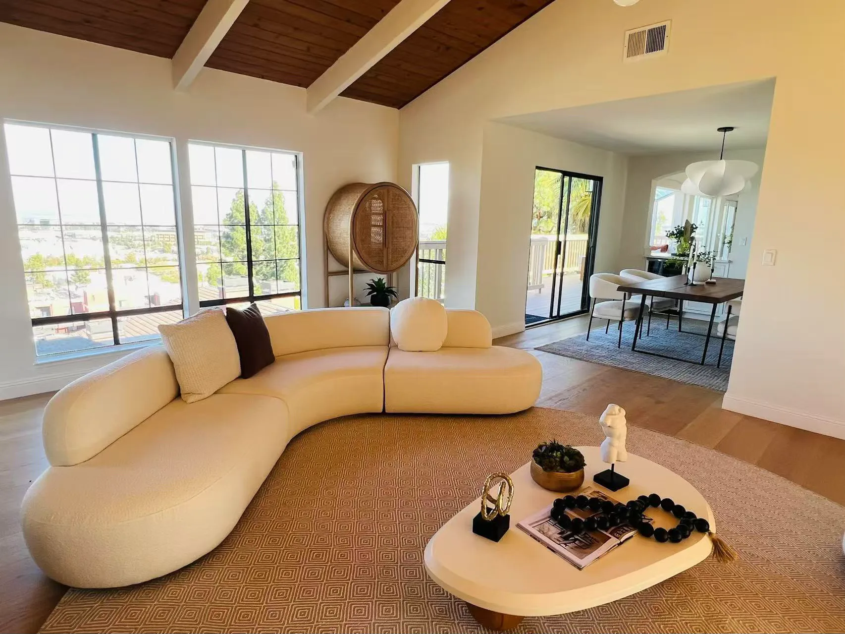 Sunlit open-plan living room with a curved sofa, fireplace, and exposed ceiling beams