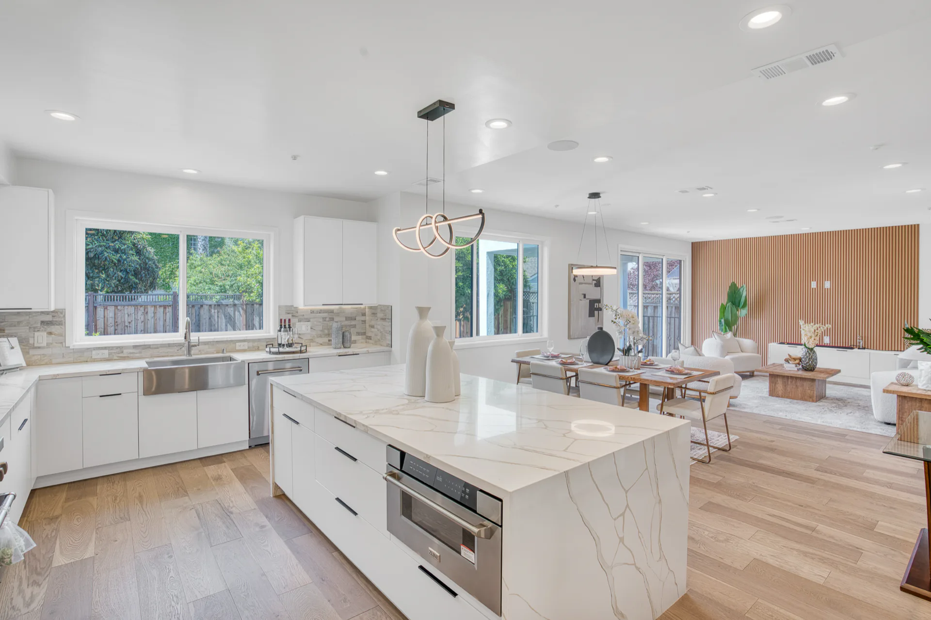 White kitchen remodel with an oversized island, range hood, and open living area