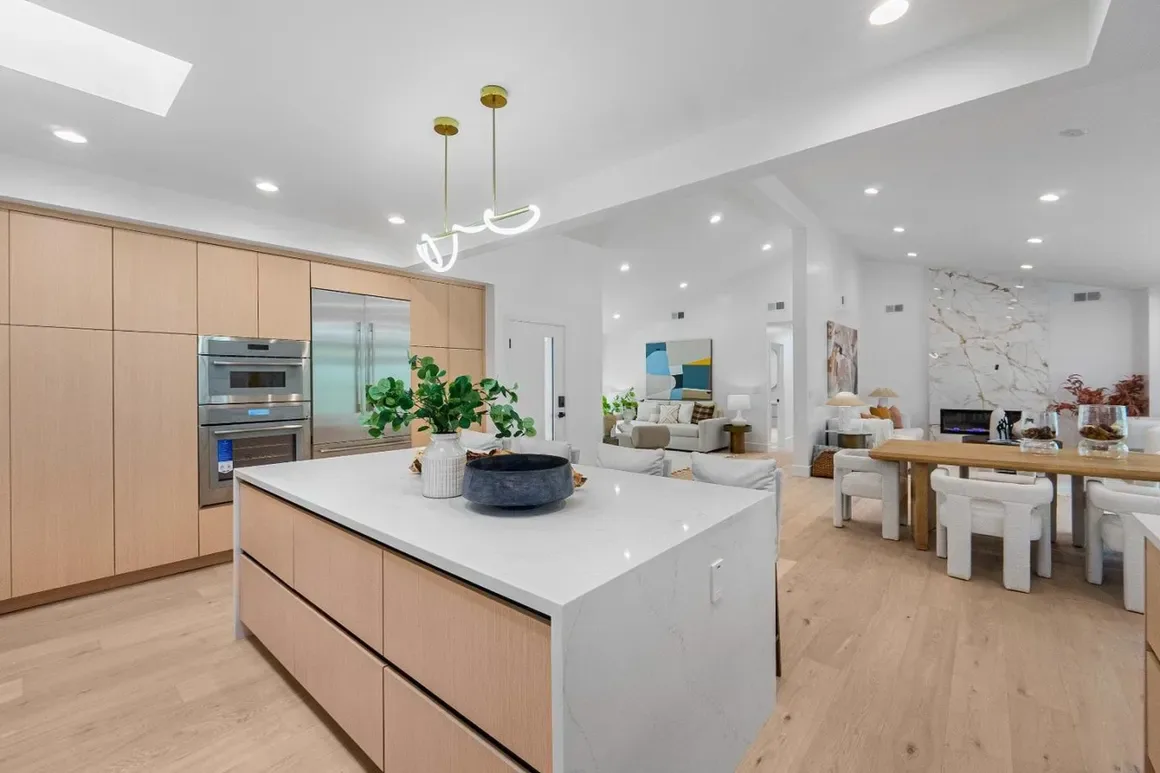 White oak kitchen with a waterfall island, integrated appliances, and open dining area